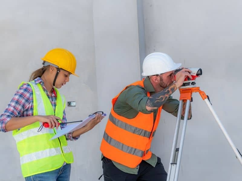 Land surveyor reviewing updated survey records at a redevelopment site with abandoned pavement, former building foundations, and existing utility features.
